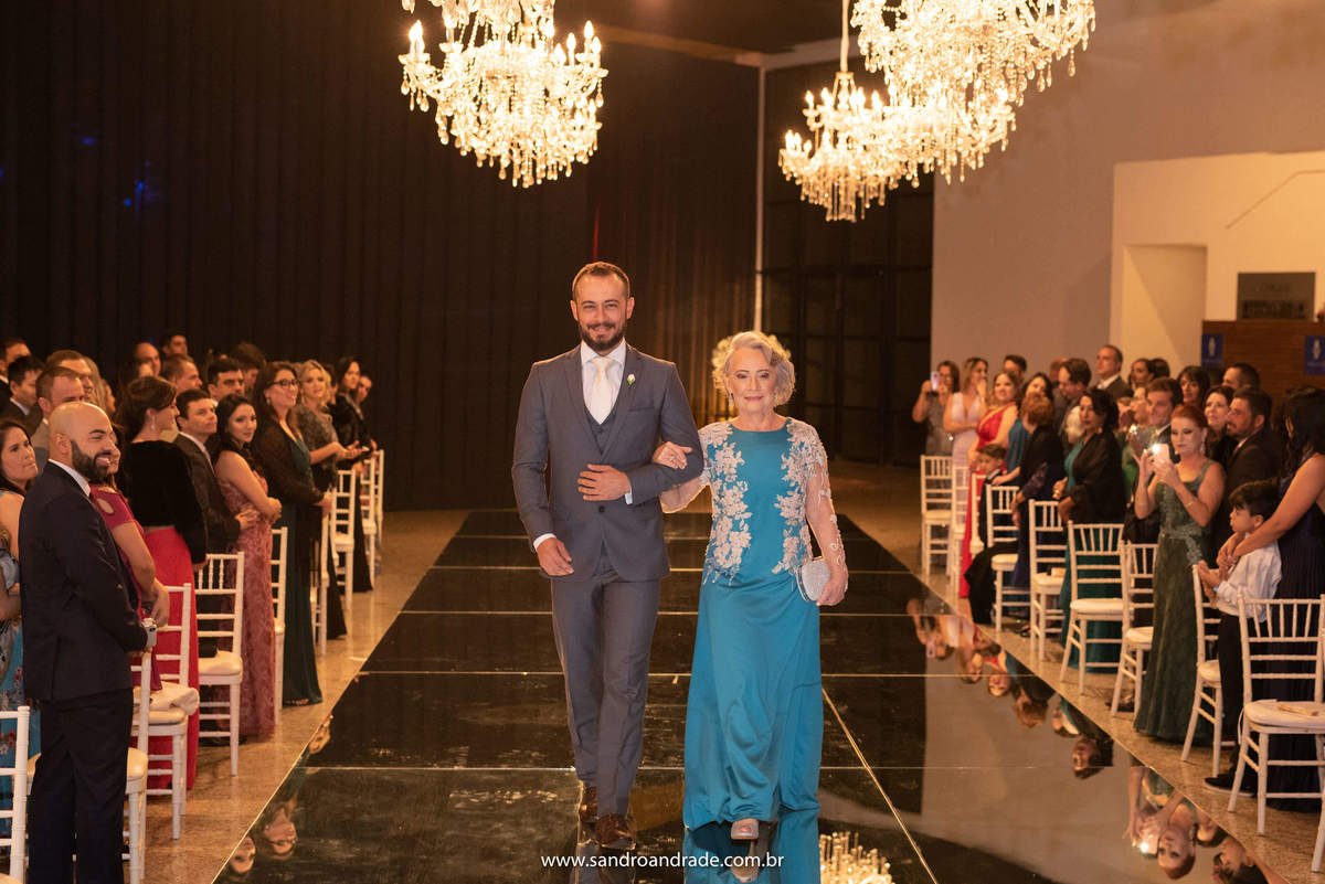 O noivo de braço dado com sua mãe, fazendo sua entrada triunfal.