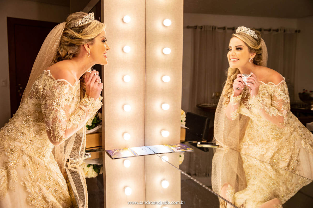Cassia se vestiu na suite da noiva no espaço Unique, nesta fotografia, temos o reflexo e a noiva duplicada passando perfume, com toda a luz do espelho da suíte.