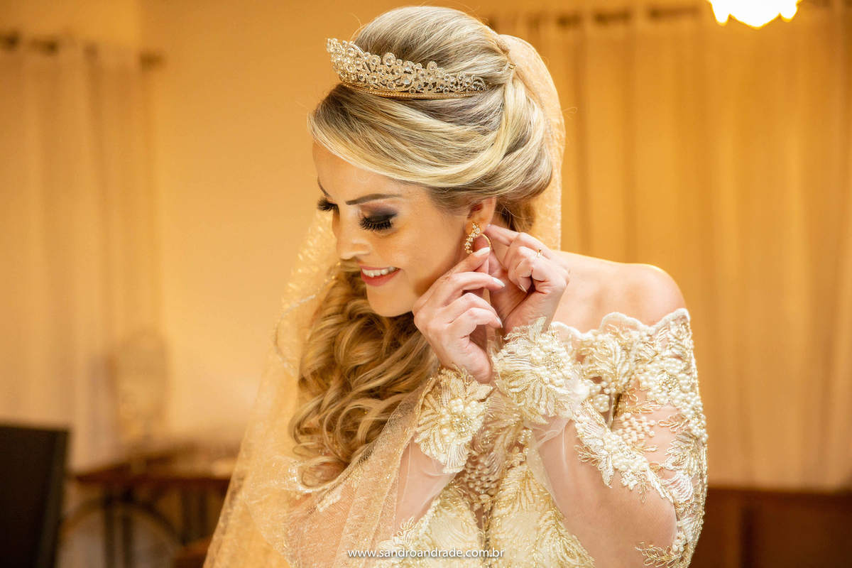 Retrato da noiva colocando o brinco, fotografia colorida. Brincos e coroa de Consuelo Piñon.