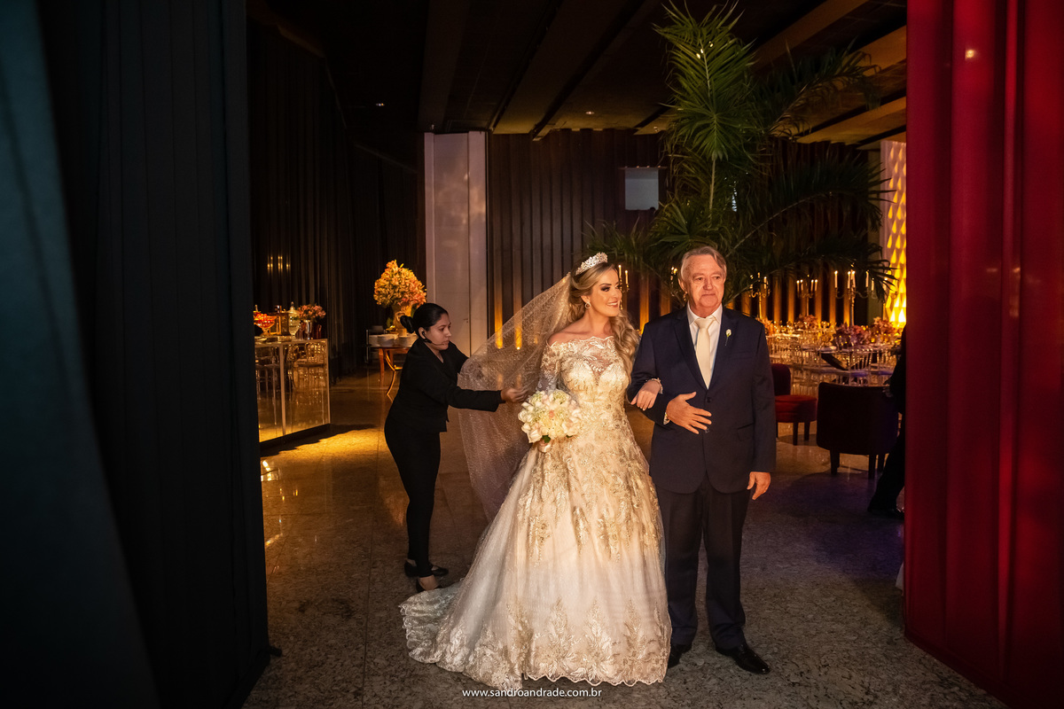 Cassia está de braço dado com seu pai, muito emocionados, só aguardando a vez deles entrarem.