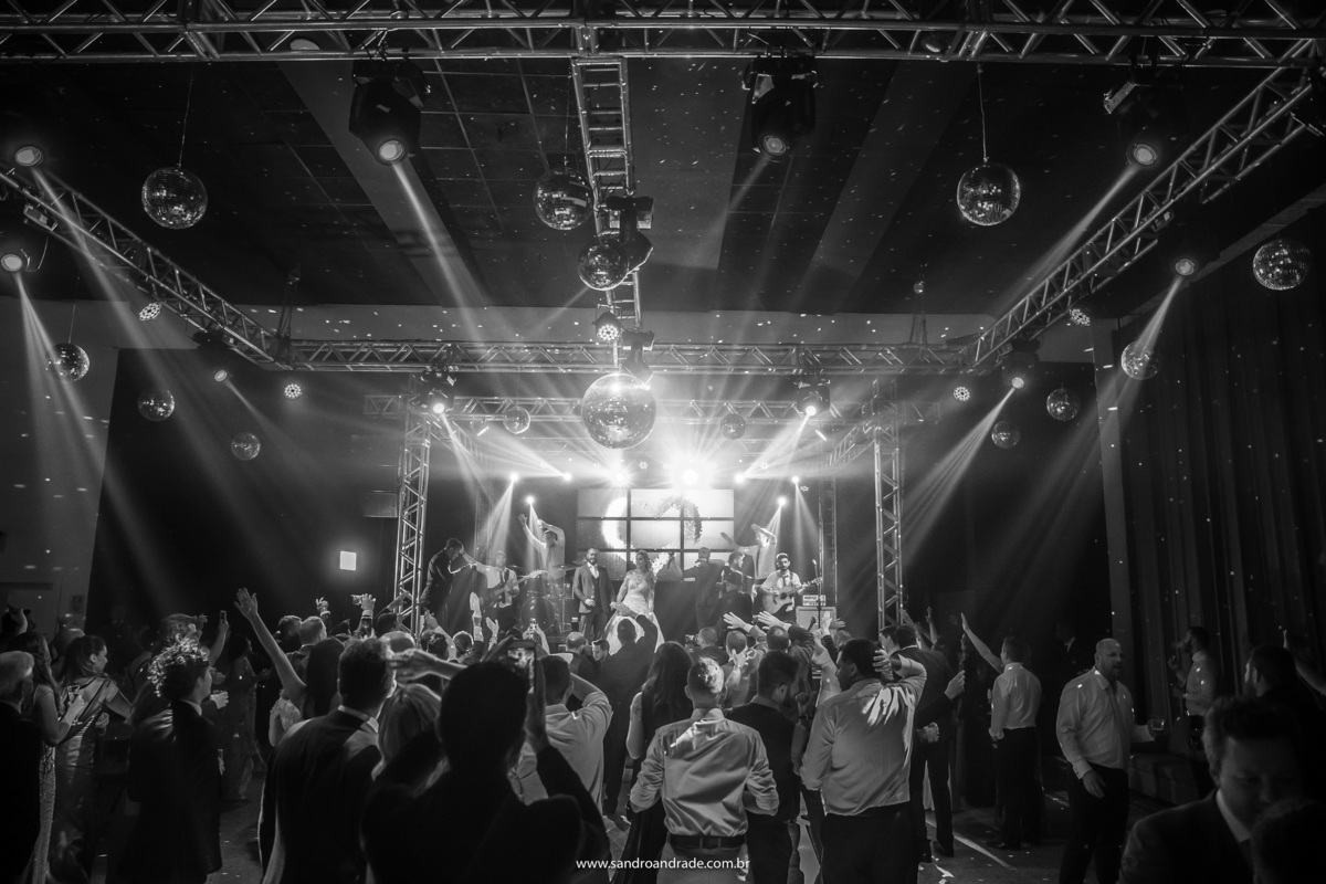 Na fotografia preto e branco, uma imagem da boate toda com os noivos ao fundo em cima do palco.