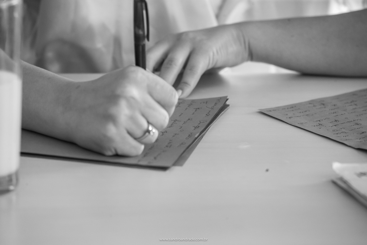 Fotografia de detalhes, a mão da noiva com seu lindo anel de noivado, escrevendo os votos. Fotografia preto e branca perfeita, feita pelo fotógrafo de casamentos Sandro Andrade, nosso artista.