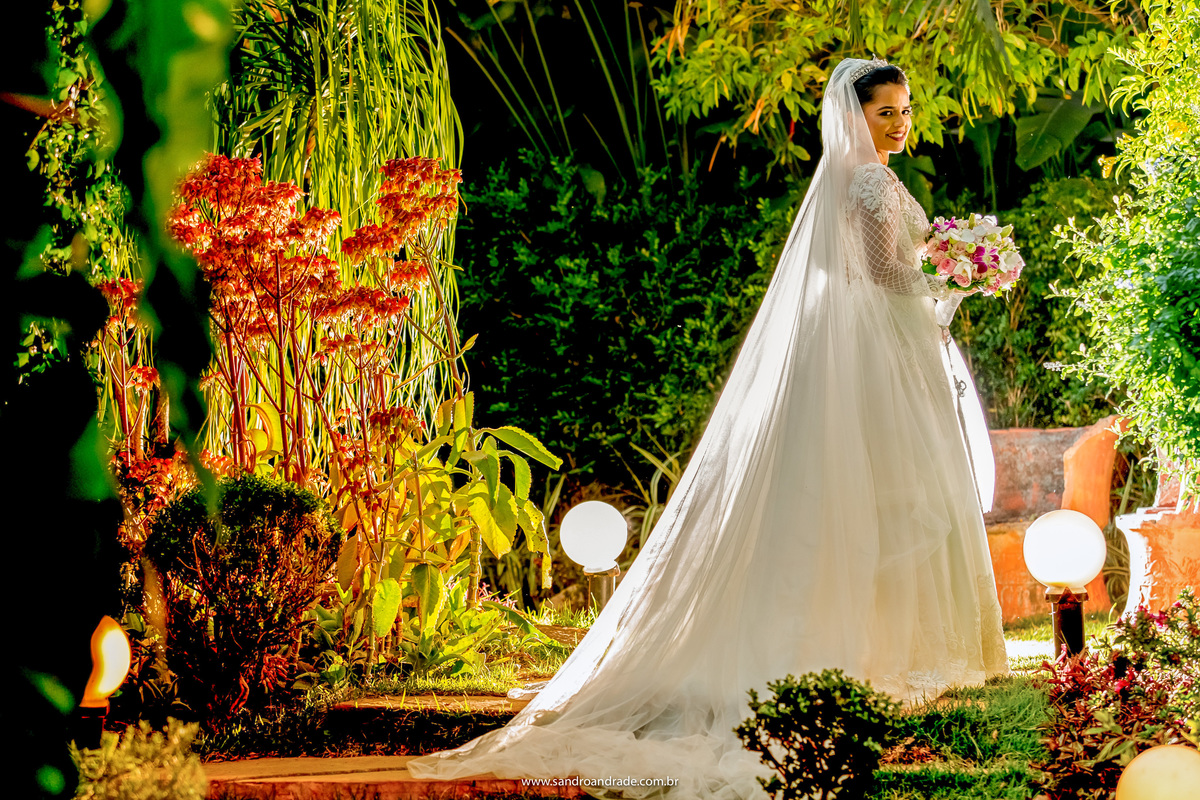 No meio do jardim, entre as luminárias, Flavia está de costas e dá uma olhadinha para as lentes do nosso artista Sandro Andrade, fotógrafo de casamentos no DF.