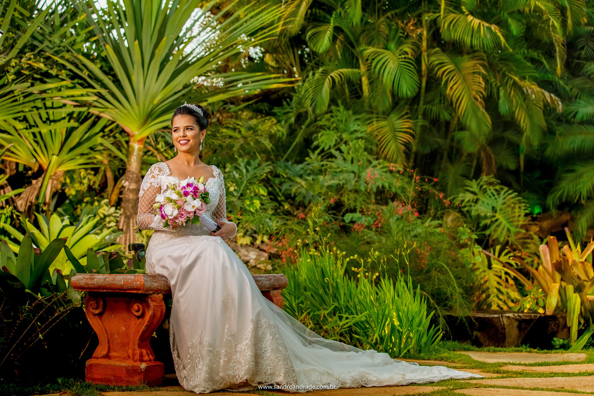 Sem o véu, Flavia está sentada no jardim com seu buque na mão em uma linda fotografia colorida.