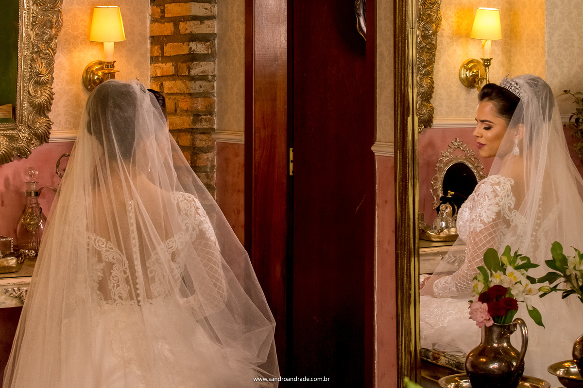 No quarto da noiva, de olhos fechados e pensando no grande dia que está chegando, Flávia está de costas e seu reflexo de frente no espelho.