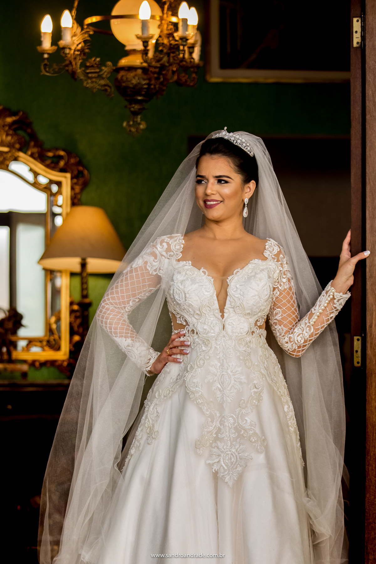 Uma linda imagem colorida, a noiva está sorrindo, em pé segurando na porta do quarto da noiva.