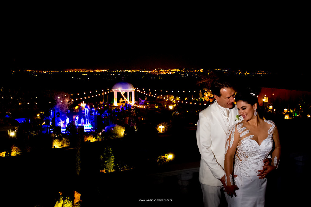 Os noivos apaixonados e sua festa ao fundo, vista do lago