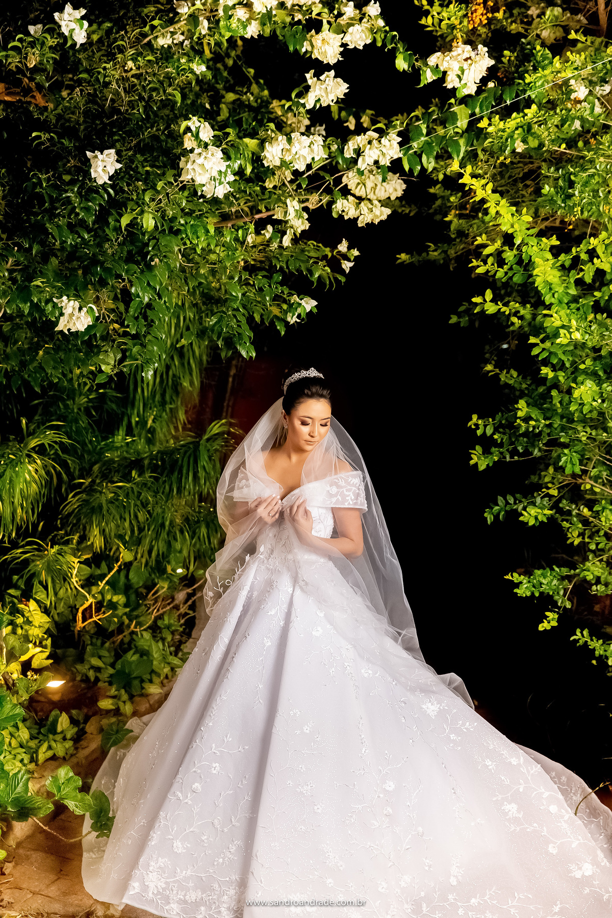 Ainda no mesmo local, agora ela segura seu véu ou casquete e olha para baixo, muitas bouganvileas em cima e todos os detalhes do vestido da noiva bem visíveis.