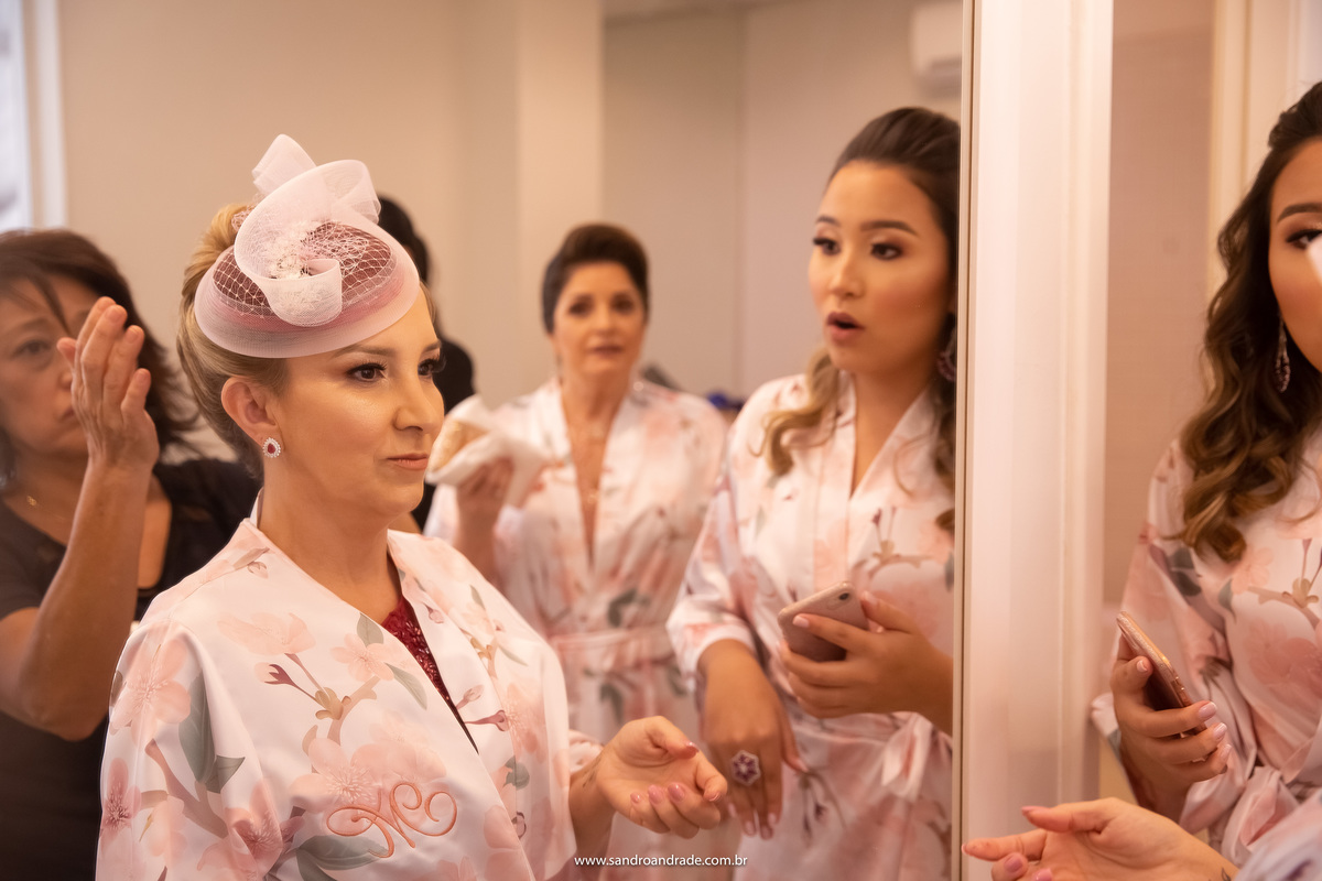 Mamãe na frente do espelho fazendo os ajustes no seu penteado, enquanto a sogra de sua filha da alguns palpites ao da sua outra filha.