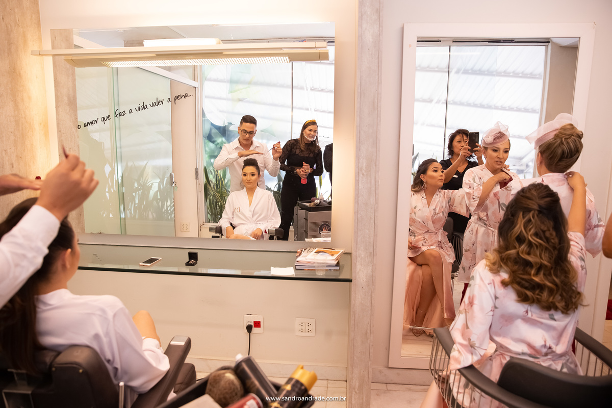 Uma imagem bem criativa e de uma composição maravilhosa, por Sandro Andrade fotógrafo de casamentos do DF. No espelho ao lado esquerdo temos a noiva atentamente no penteado e ao  lado direito, está a Keith e a sua mãe fazendo os ajustes no roupão dela.