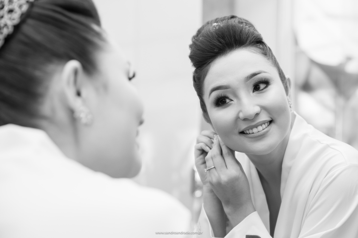 A noiva colocando seu lindo e delicado brinco em frente ao espelho.