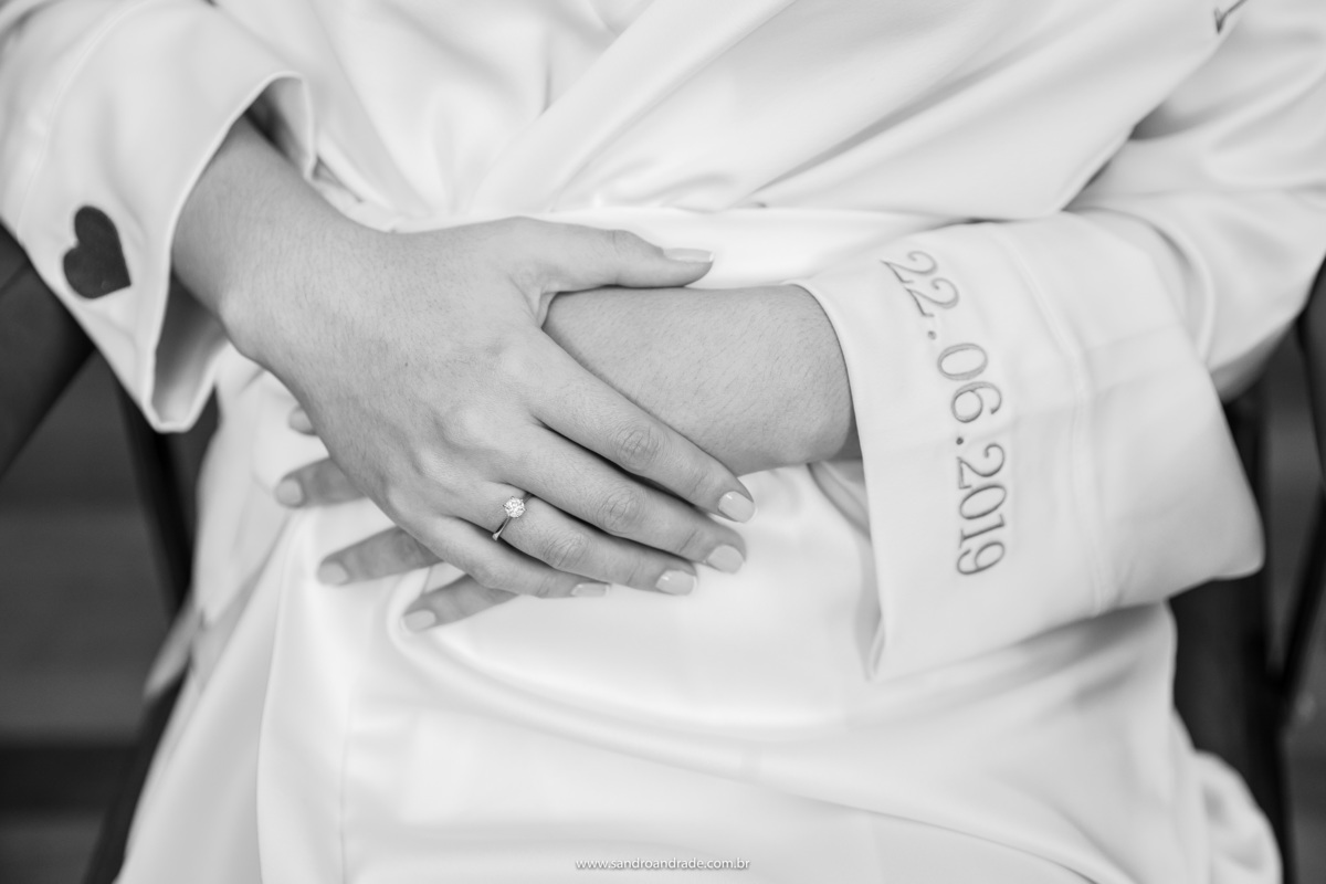Em detalhe o roupão da noiva, com um coração bordado e a data do casório e um lindo anel de noivado em sua mão direita.