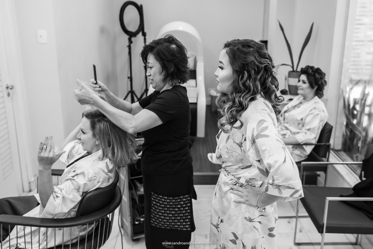 A mãe da noiva agora está produzindo o cabelo, sob os olhares da filha, conferindo se tudo está do jeitinho que elas querem.