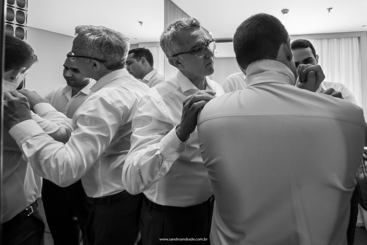Nesta fotografia o noivo está recebendo a ajuda do pai e dos irmãos para colocar as abotoaduras, um click de momento em que Sandro Andrade fotógrafo de casamentos em BSB se espreme atras deles para conseguir fazer este click.