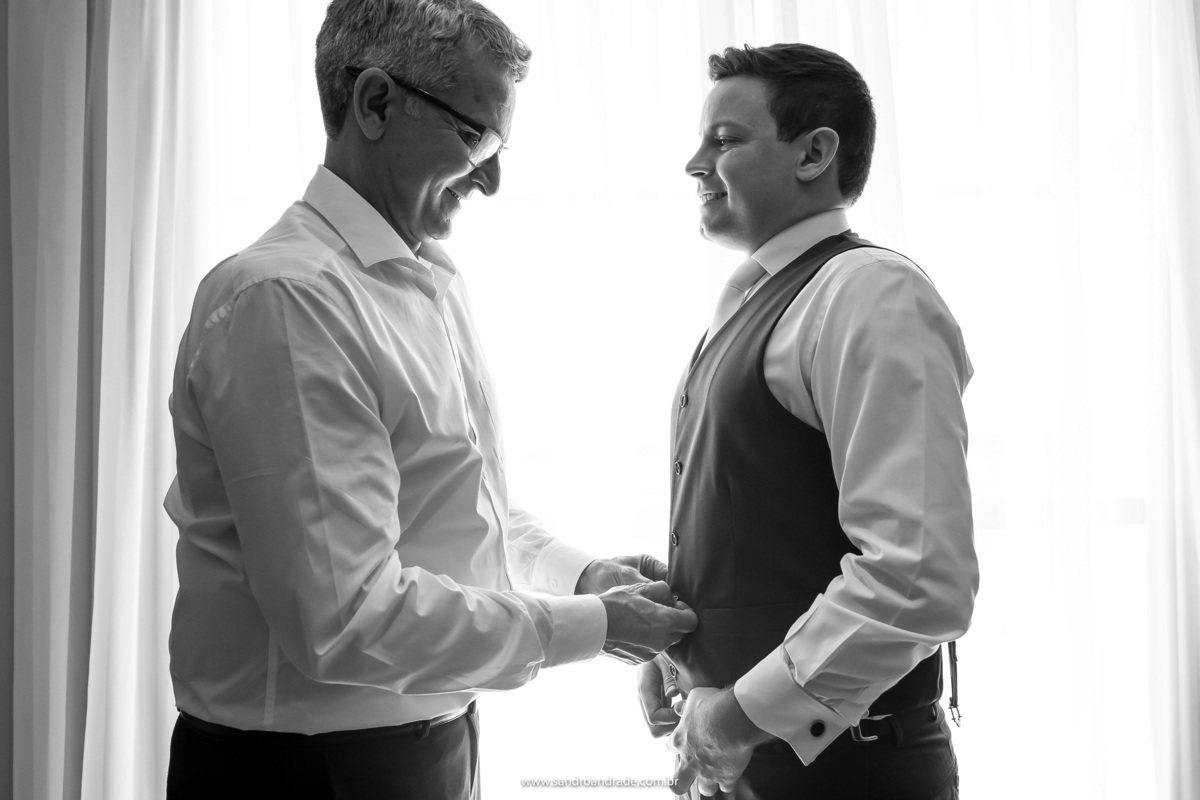 Com a ajuda de seu pai, o noivo Murilo fecha o colete que compõe seu look de noivo, um terno muito lindo da máxime noivos e black tie.