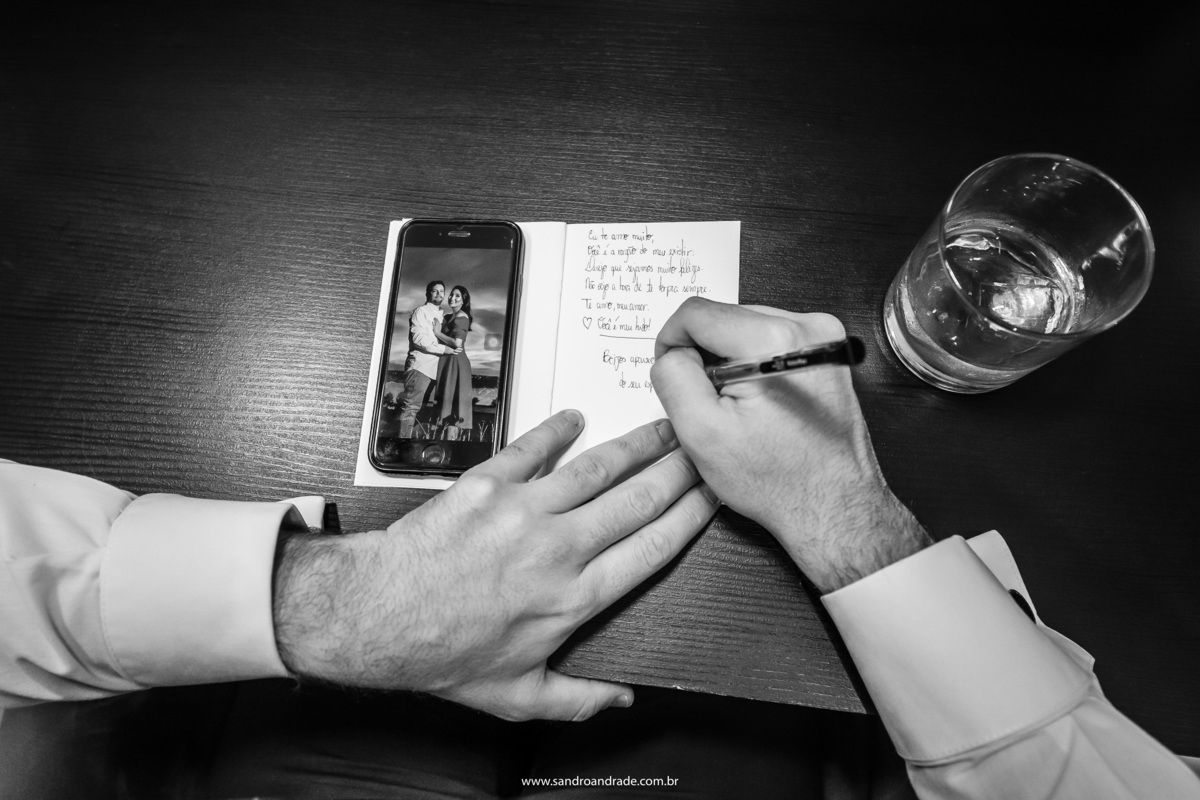 Fotografia de detalhes, feita por Sandro Andrade fotógrafo do DF. I noivo está escrevendo os votos e o telefone está ao lado mostrando uma fotografia do casal.