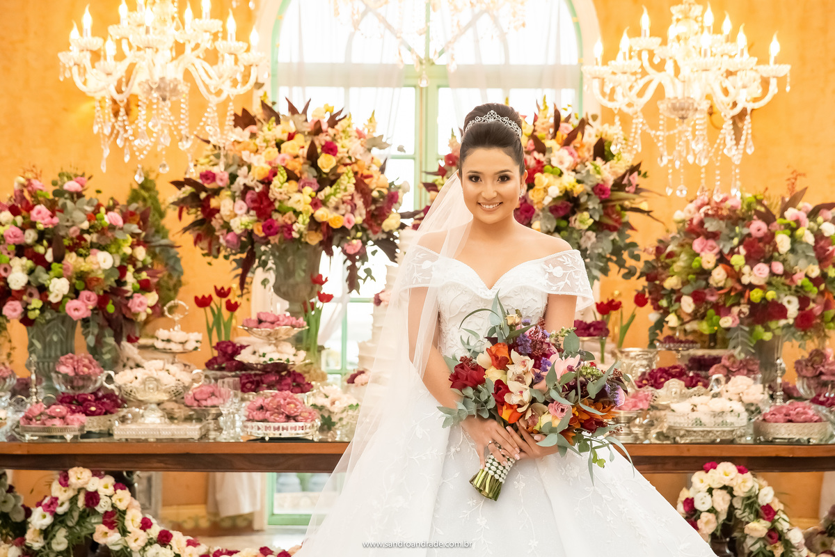 Dany esta de frente para Sandro Andrade seu fotógrafo, sorrindo e posando para fotos na mesa do bolo.