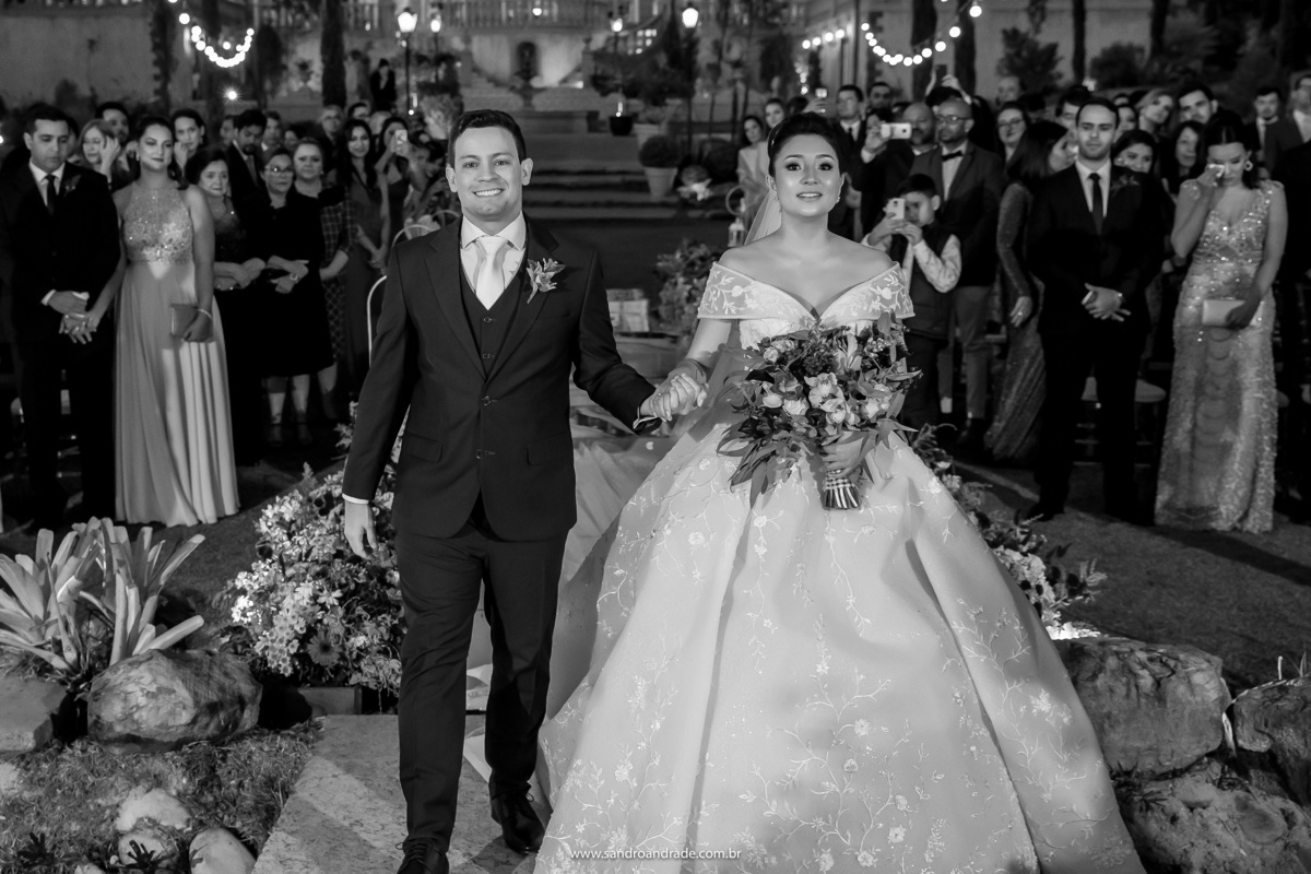 O casal feliz, de mãos dadas indo para o gazebo, onde o pastor aguarda para celebrar a união dos dois.