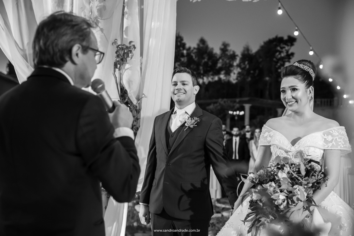 O casal sorri enquanto o pastor fala com eles e elogia o quanto os dois estão bonitos.