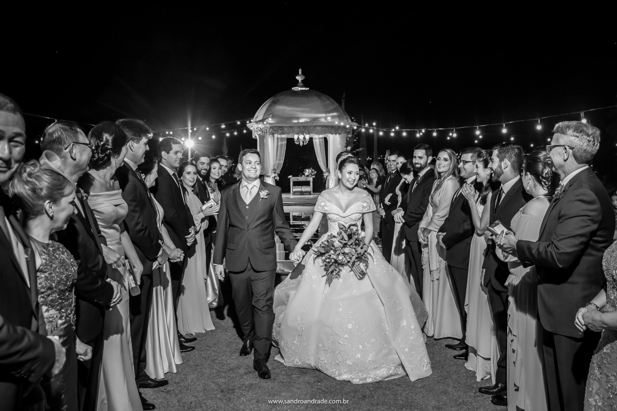 Uma linda fotografia em preto e branco da saída dos noivos, sorrindo, felizes e muito descontraídos, Sandro Andrade um dos melhores fotógrafos de casamento não perde nenhum momento e tudo sob o olhar atento do pai da noiva, que está observando tudo. risos