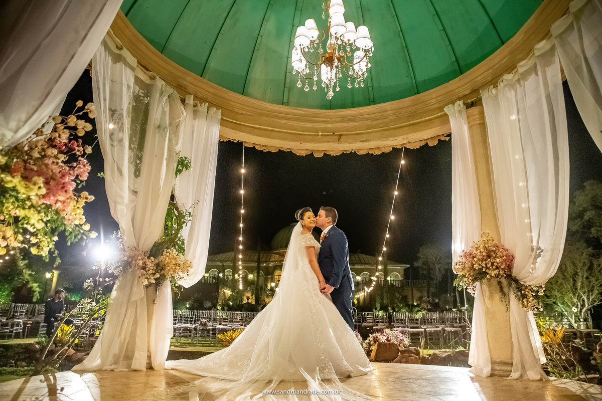 Linda fotografia do casal dentro do gazebo, bem iluminada, um casal apaixonado e com amor Murilo beija no rosto de Dany, não é a toa que Sandro Andrade é entitulado por Dhyana Giardini, dona da Villa Giardini e decoradora do espaço, como O MESTRE DA LUZ.