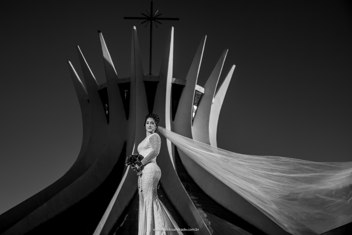 A noiva está sozinha nesta fotografia preto e branco, na frente da catedral e o véu voando.