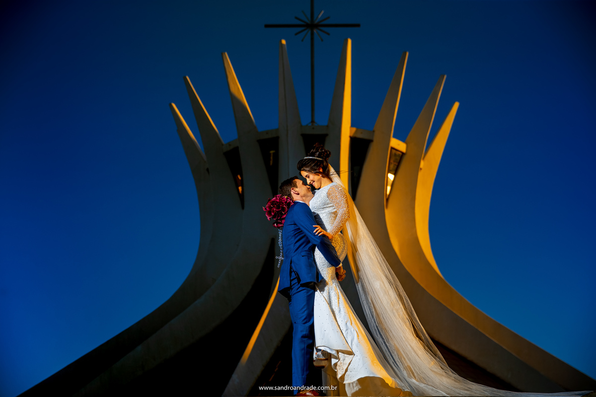 Não é a toa que Sandro é um dos melhores fotógrafos de casamento bsb, nesta fotografia ele colocou Wedson para pegar Mayara no colo e ergue-la, com um olhar apaixonado eles quase se beijam, nesta linda imagem colorida o sol bate de um lado da catedral.