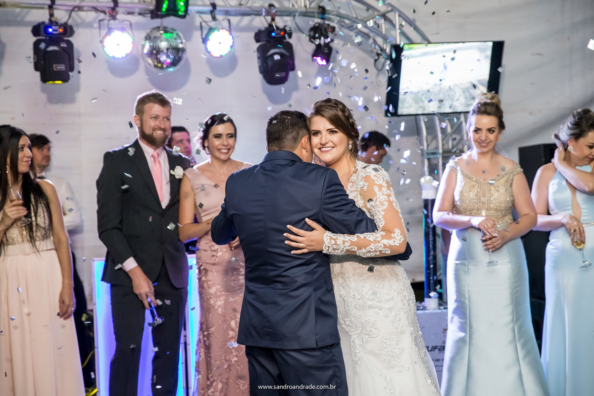 Agarradinhos e felizes, os convidados e padrinhos sorriem.