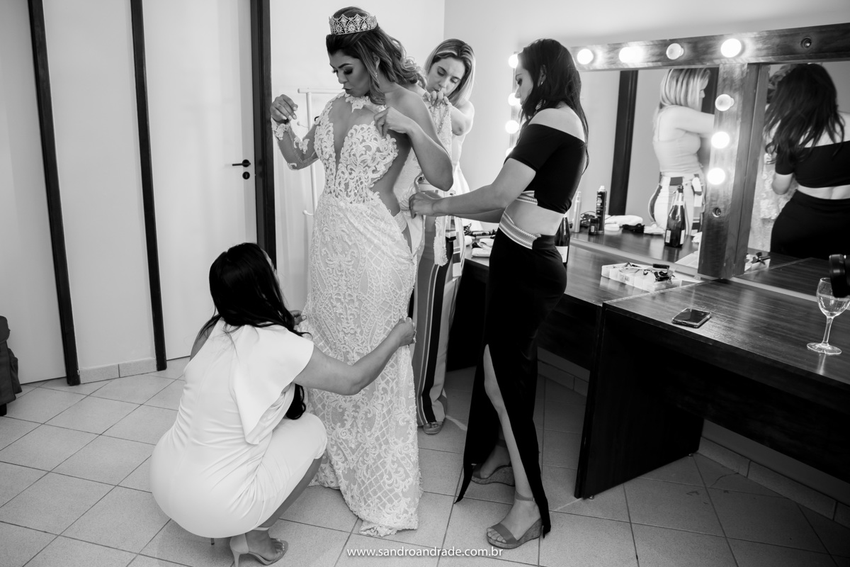 Agora vestindo seu vestido de princesa sensual, marcando bem o corpo, sendo arrumado na parte da frente por sua irmã e melhor amiga, enquanto a maquiadora e cabeleireira estão arrumando o vestido nas costas.