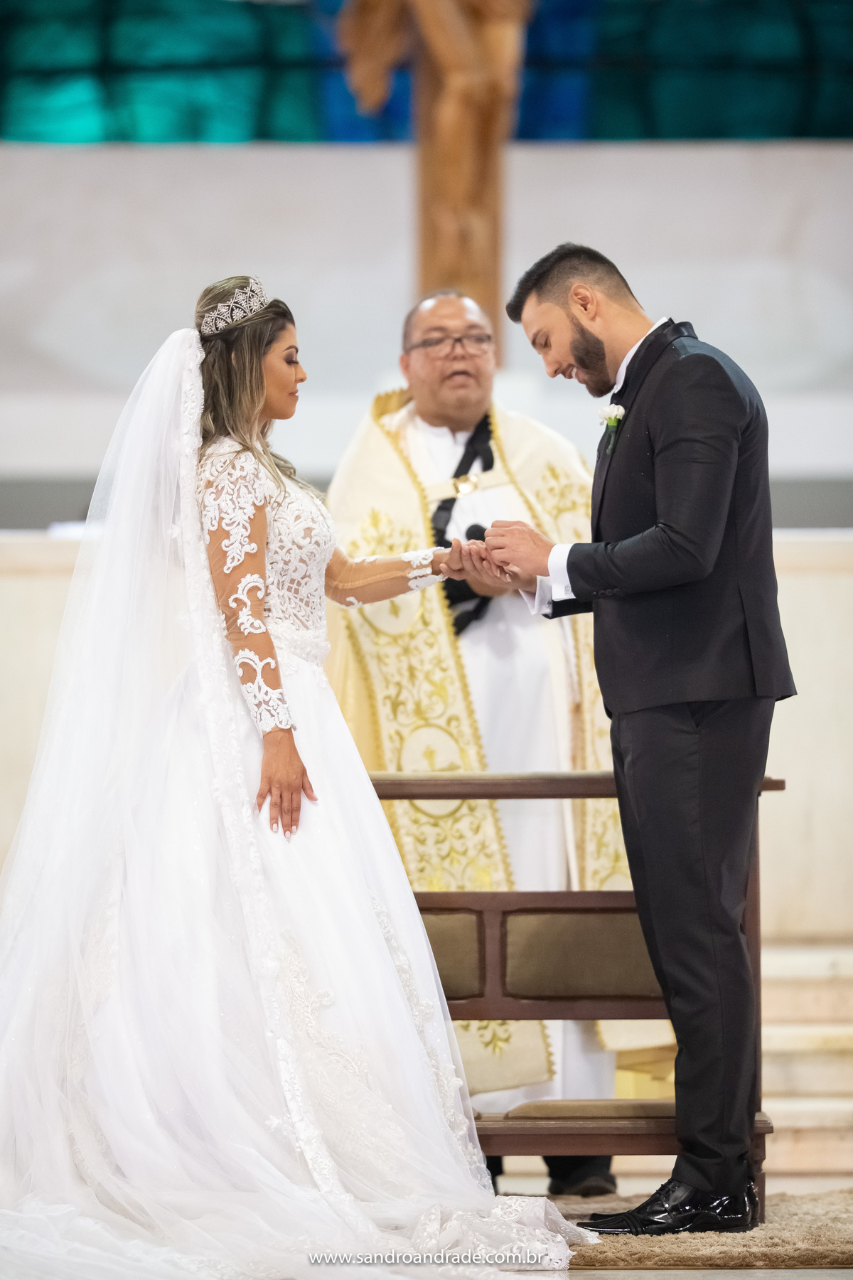 Sandro e Wanessa estão de frente um para o outro, ele então coloca a aliança em seu dedo.