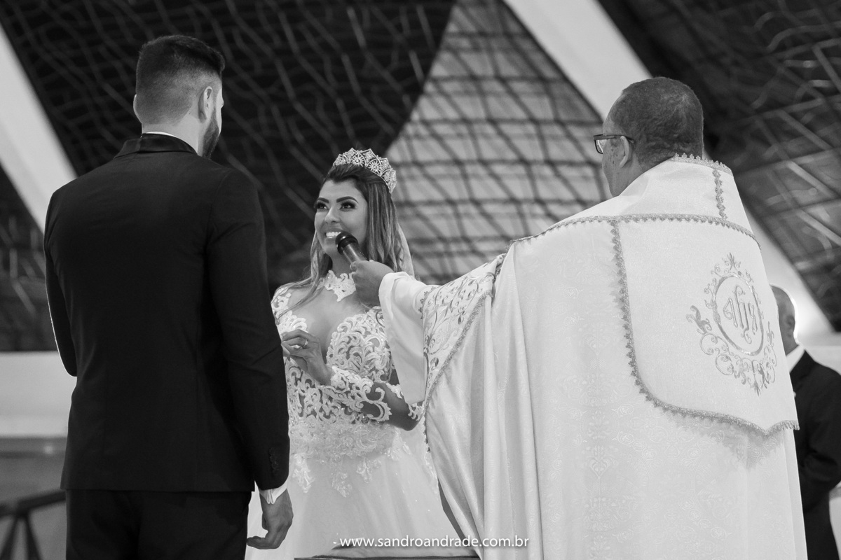 De um angulo diferente a noiva está fazendo as juras ao seu grande amor e colocando a aliança em seu dedo.