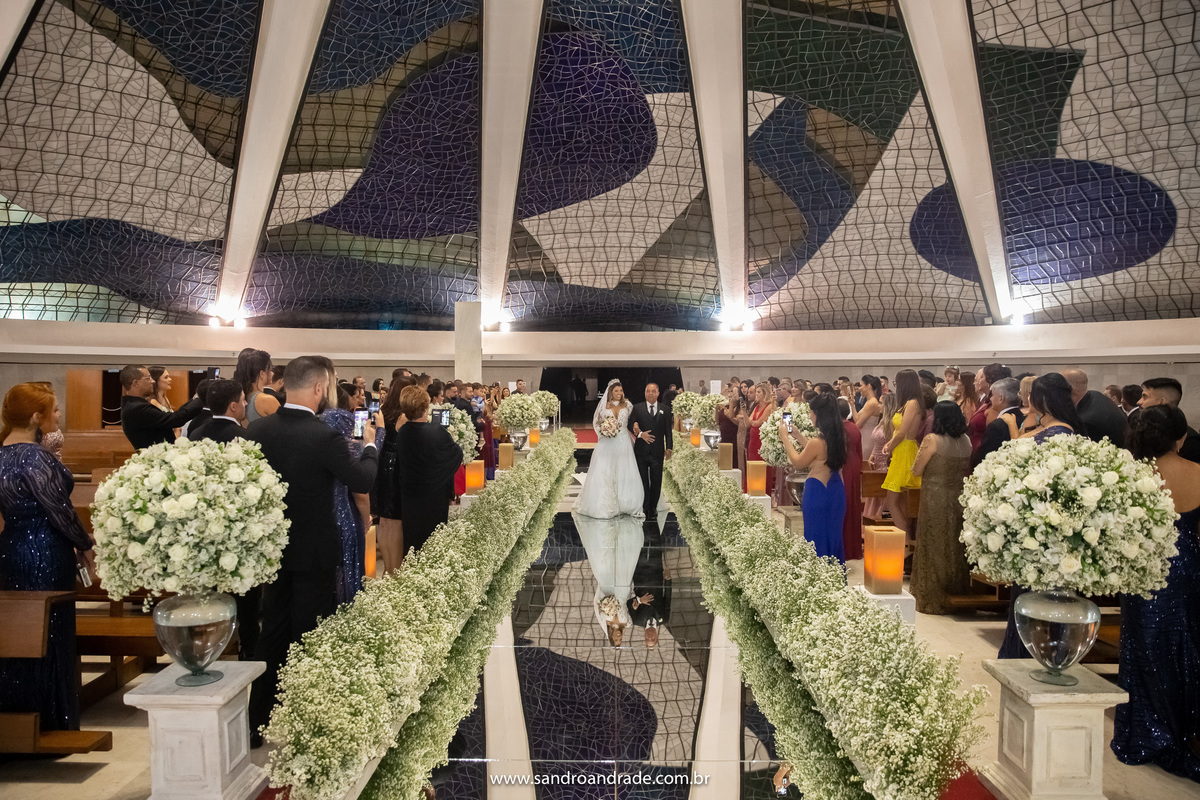 A entrada da noiva ao lado de seu amado pai, uma fotografia bem, aberta pegando toda a igreja e os convidados nos bancos.