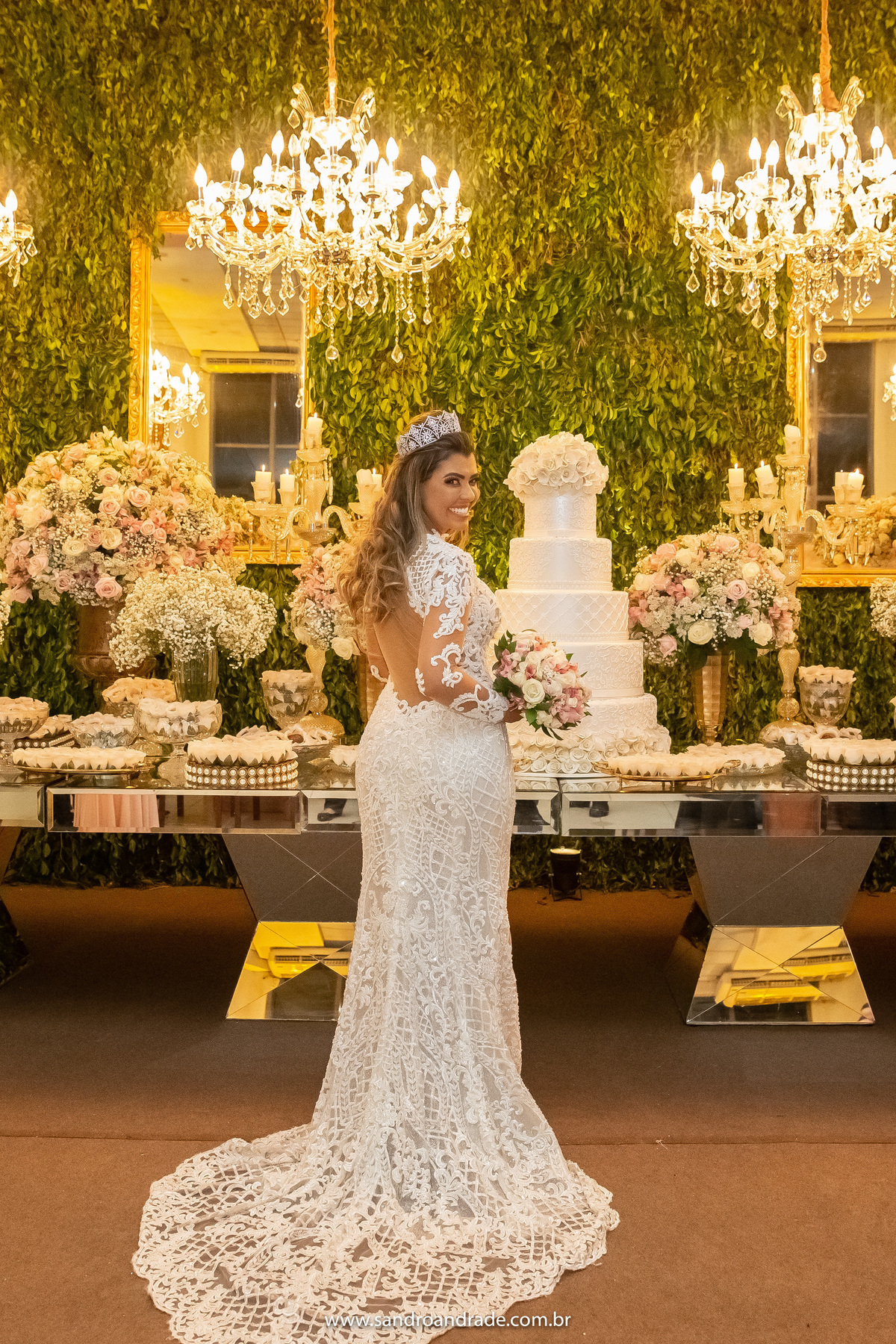 A noiva está um pouco de costas, sem o véu, já mostrando os detalhes das costas de seu lindo vestido de noiva todo em renda do Atelier Maria Virginia e jóias Consuelo Pinõn.