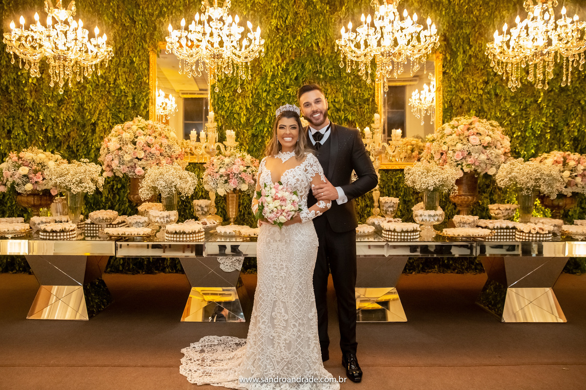 Bem tradicional na mesa do bolo, os noivos estão abraçados.