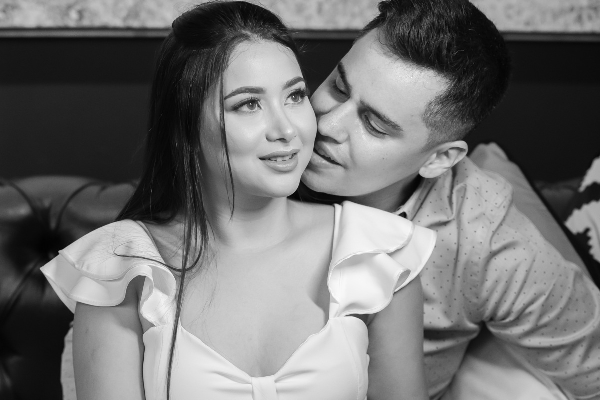 Em preto e branco, um lindo retrato do casal, o noivo está beijando o rosto de sua noiva.