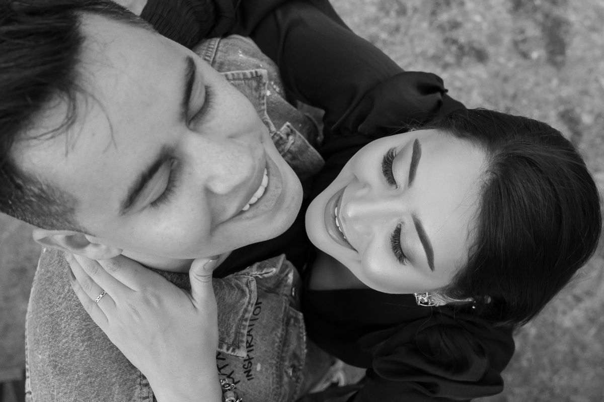 Ainda de cima, agora o rosto dos dois por completo, ambos de olhos fechados, sorrindo, em preto e branco.