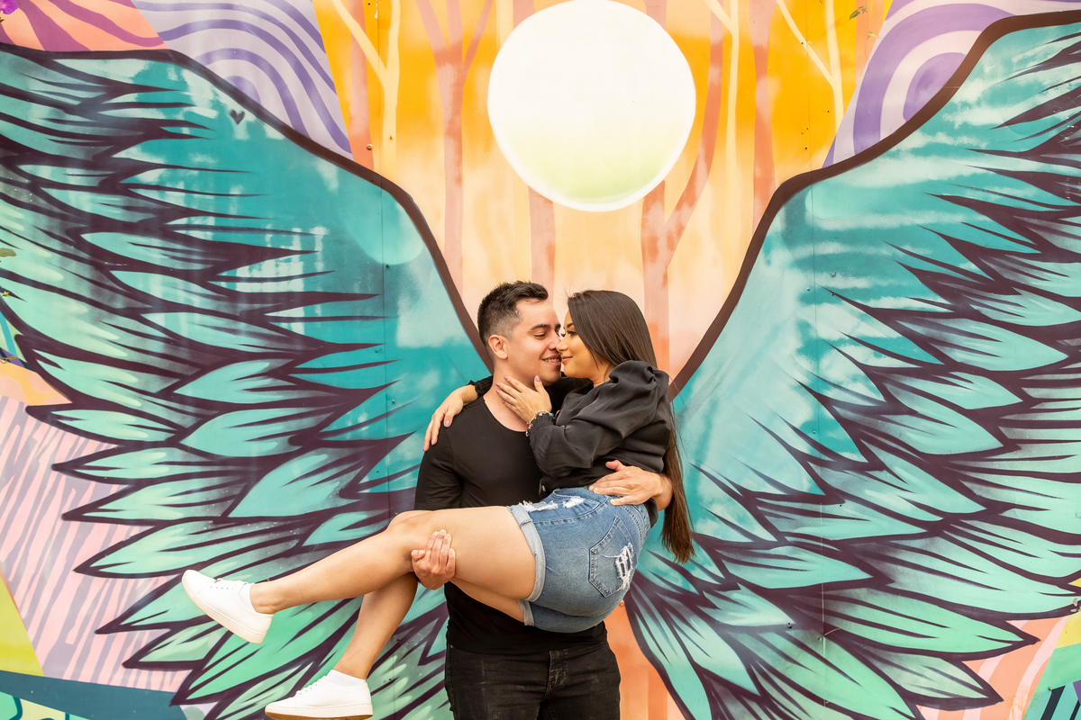 Pensa no colorido desta fotografia! Asas coloridas gigantes atrás deles e Paul está com Bárbara em seus braços, dando um beijinho no canto da boca dela.