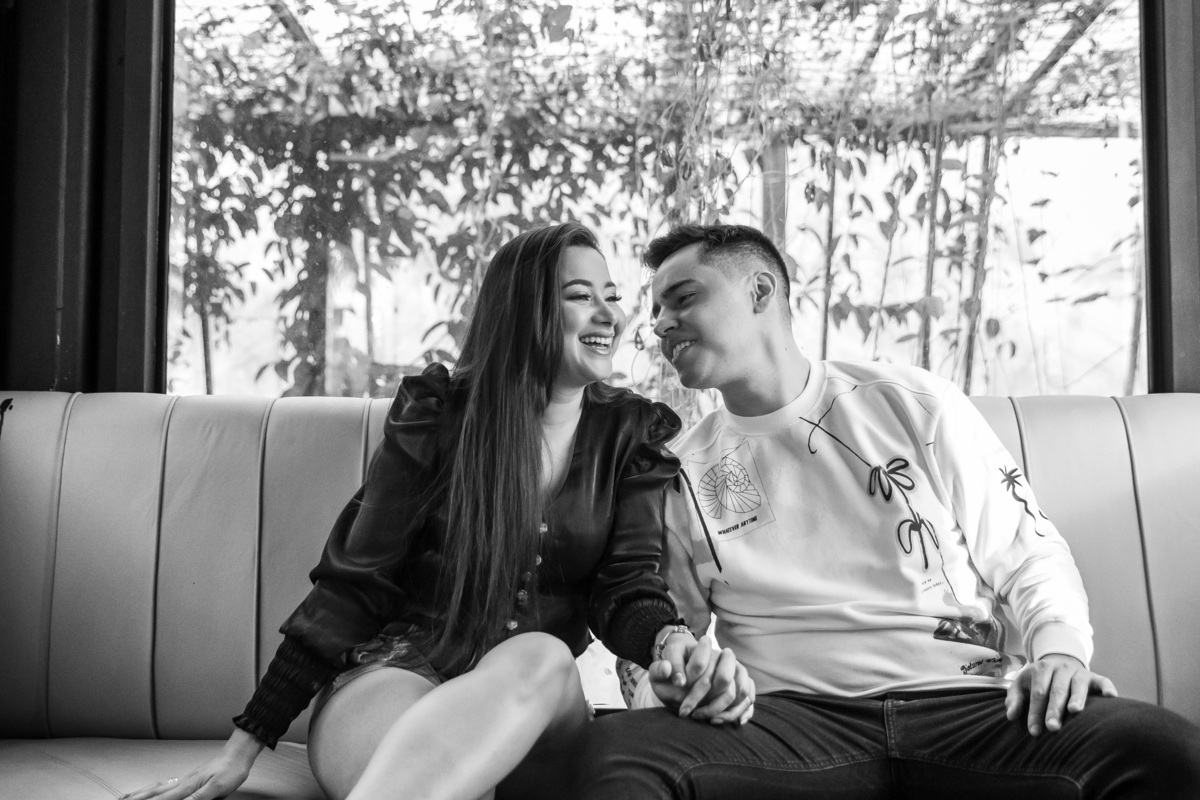 Sentados no sofá eles estão sorrindo descontraídos e já sentindo o gostinho do grande dia que se aproxima, com sorrisos bobas e conversas ao vento.