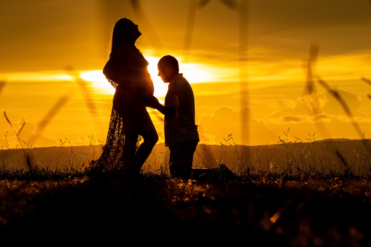 Registro gestacional muito lindo do fotógrafo Sandro Andrade, fotografo de família, gestante e casamento em Bsb. Um magnífico por do sol e uma linda silhueta, Sarah gargalhando e Renato ajoelhado tocando na linda barriga dela.