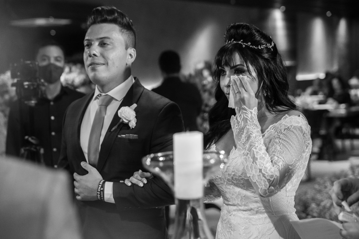 Durante a cerimonia de casamento religioso, os noivos estão de braço dado e a noiva enxuga sua lágrima.