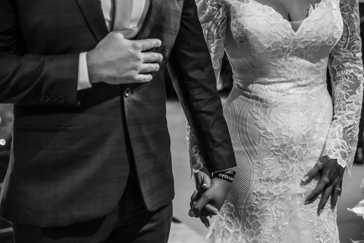 Detalhes que fazem toda a diferença e que cativa nossos noivos a cada reunião! Nesta fotografia pb, os noivos estão de mãos dadas, somente o tronco deles aparece, focando as mãos e os detalhes do vestido da noiva.