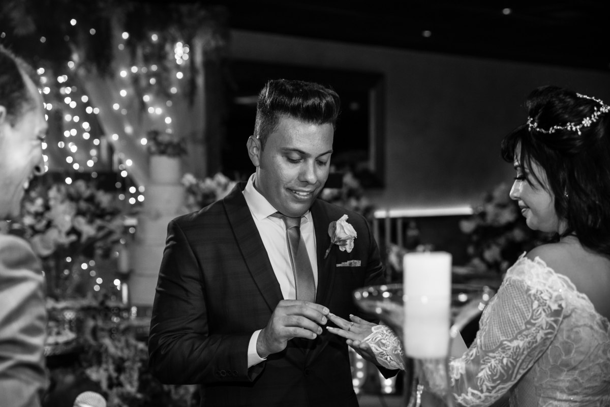 Troca das alianças..retrato dos noivos em preto e branco, em foco o noivo colocando a aliança em sua amada noiva, em segundos  esposa.