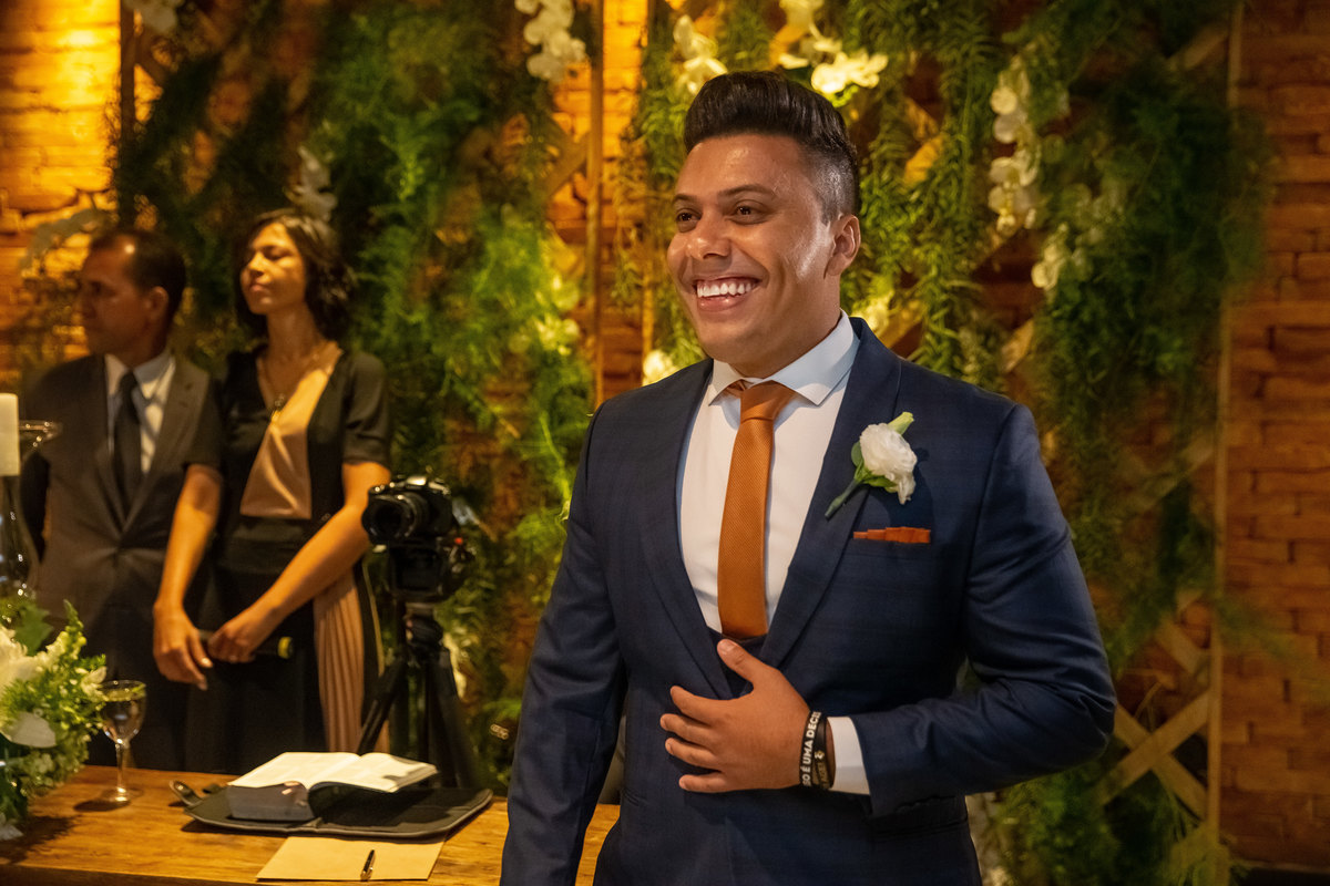 O noivo esta muito bem vestido, com um sorriso que vai de orelha a orelha e muito emocionado vendo a sua amada noiva entrando.