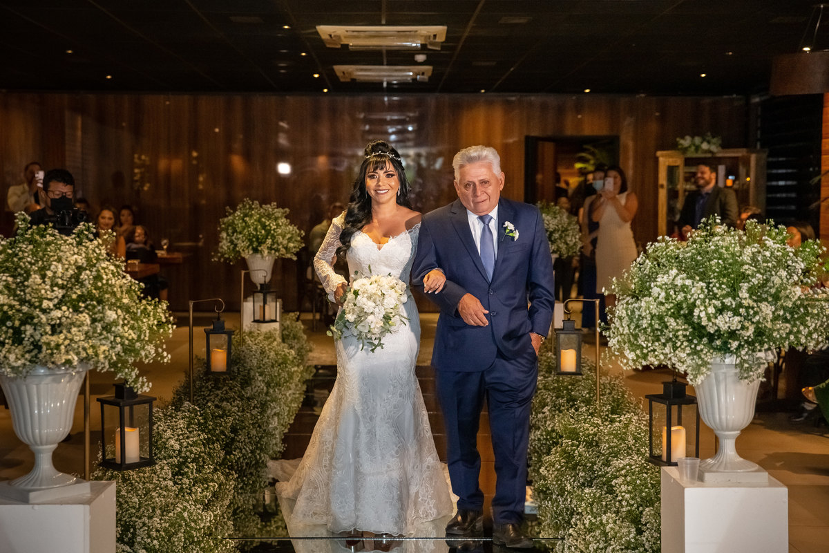 Uma fotografia de corpo inteiro da entrada da noiva com os convidados nas laterais e uma linda decoração, o coco bambu estava ainda mais bonito e aconchegante neste dia.