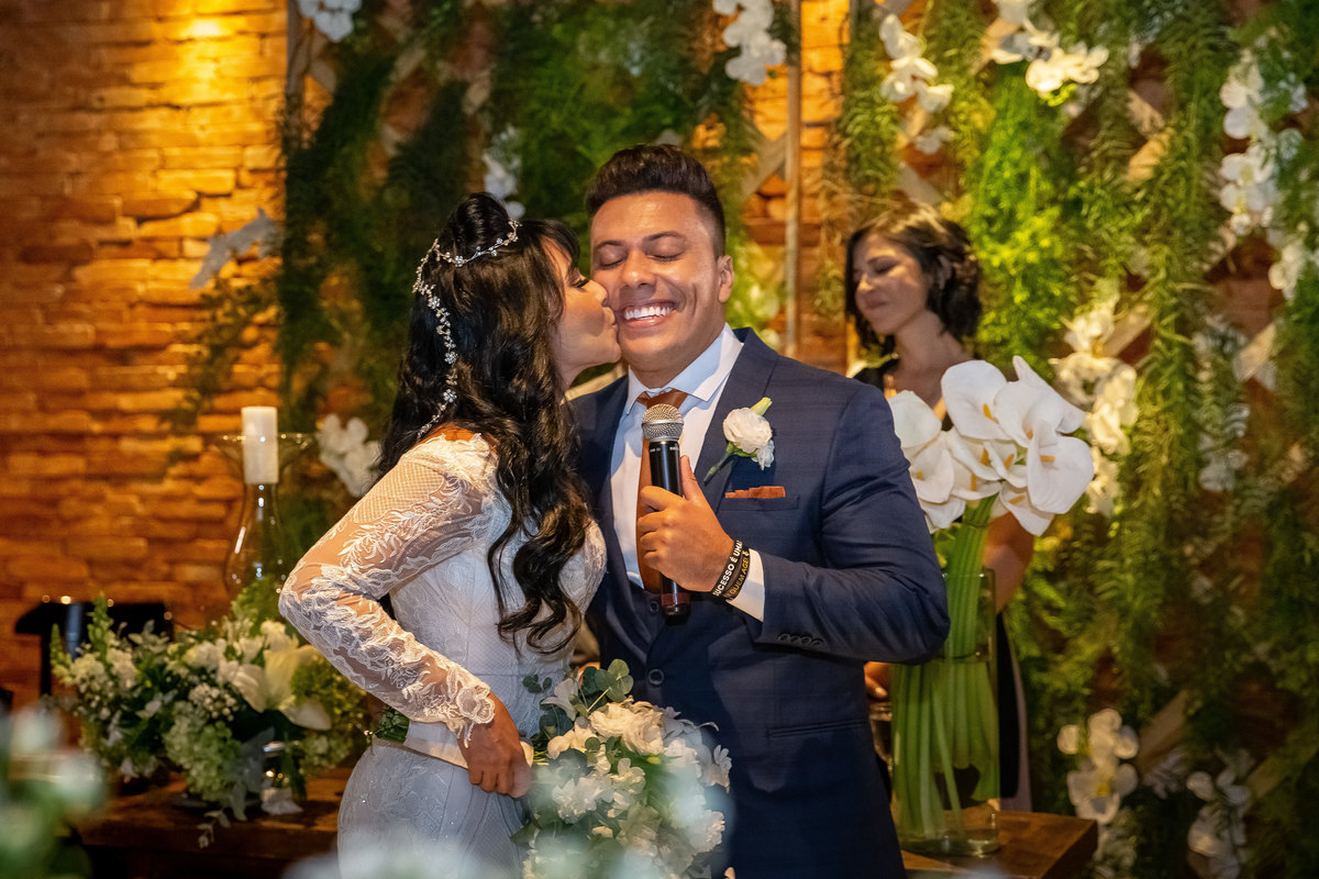 Depois de se emocionar em ver seu noivo cantando para ela, Cássia o beija no rosto e ele sorri. Um lindo retrato colorido.