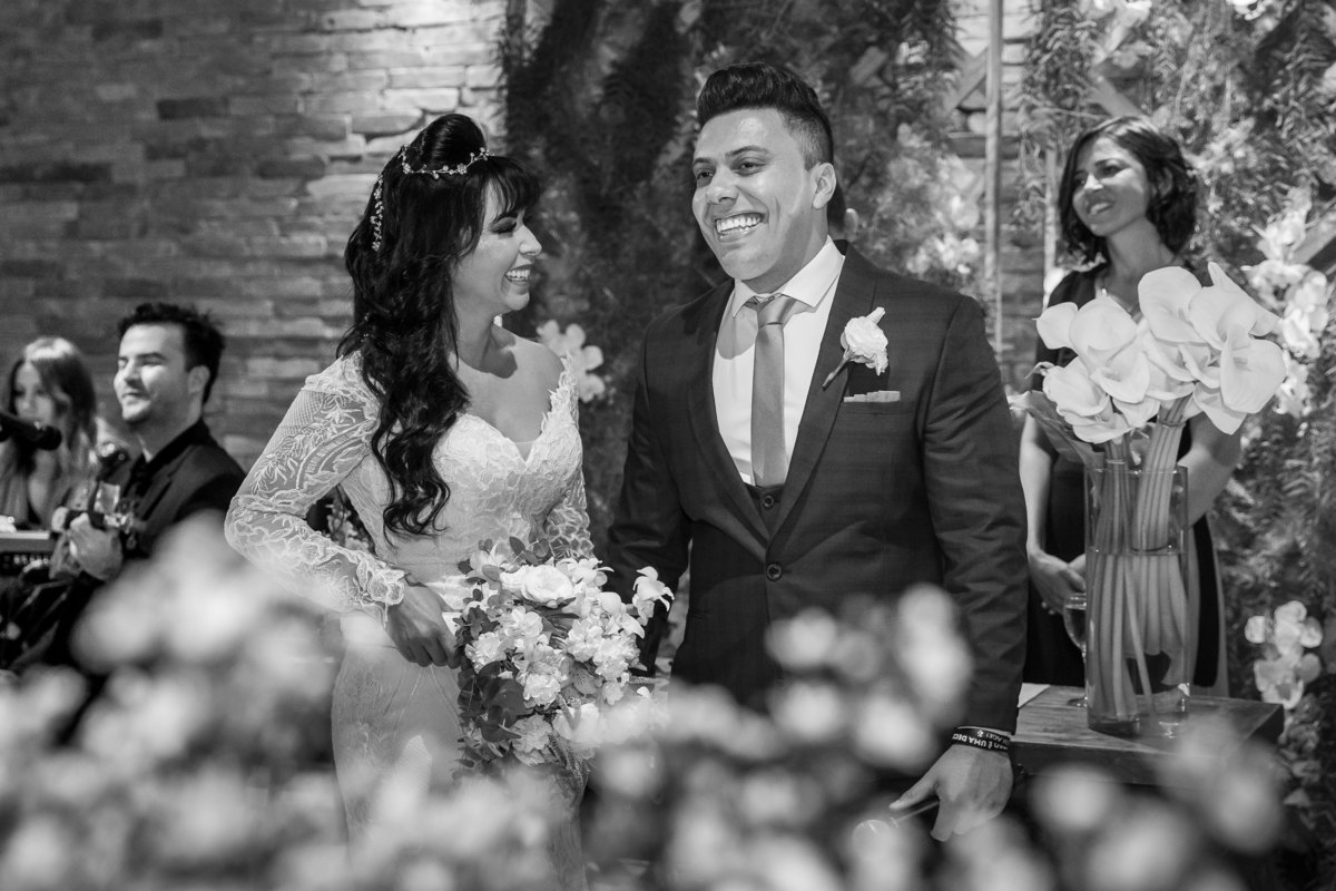 Nesta linda fotografia de momento, um preto e branco e a noiva olha para seu noivo sorrindo.