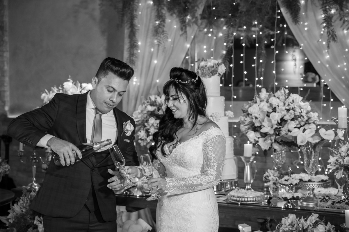 Enquanto Cássia segura as taças, Gustavo coloca o espumante nelas, uma fotografia preto e branco feita por nosso artista Sandro Andrade, fotógrafo de casamentos em Brasília.