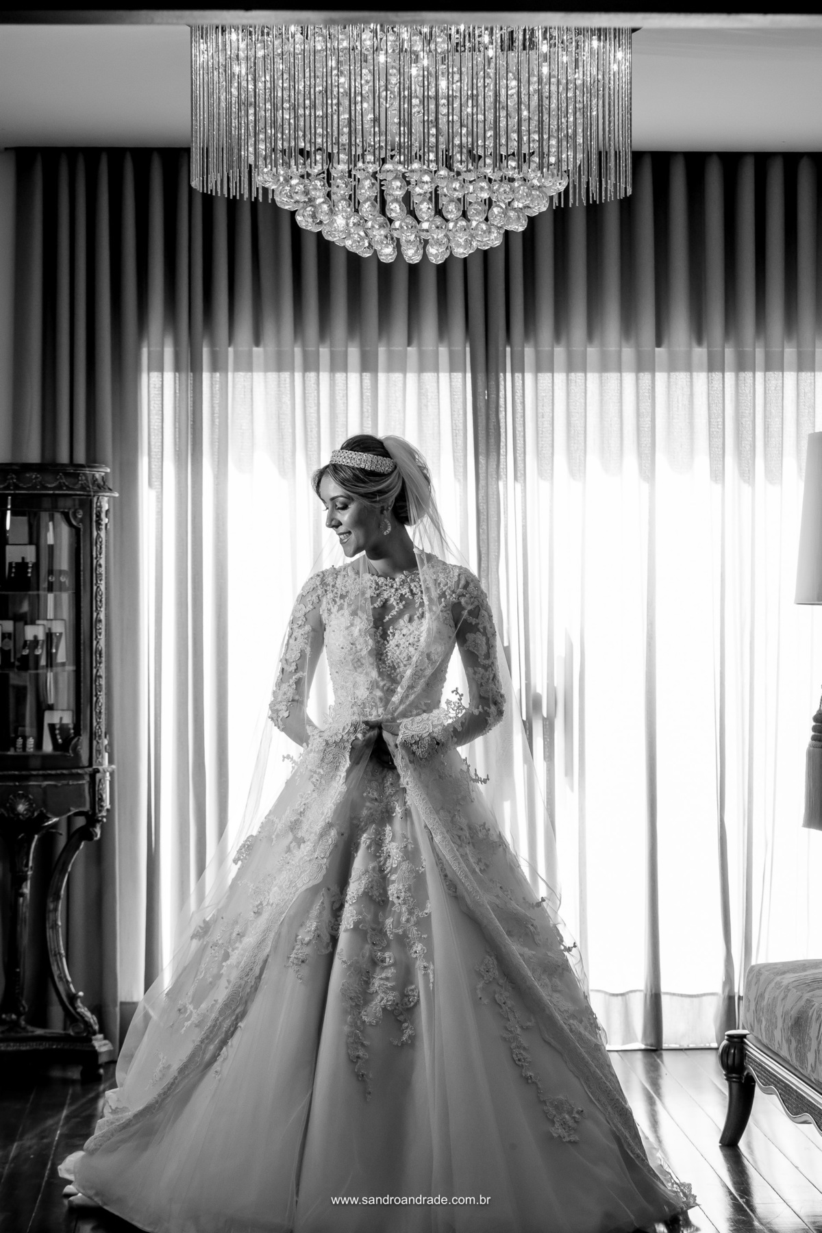 A noiva está linda, uma bela fotografia preto e branco, ela segura seu véu e sorri.