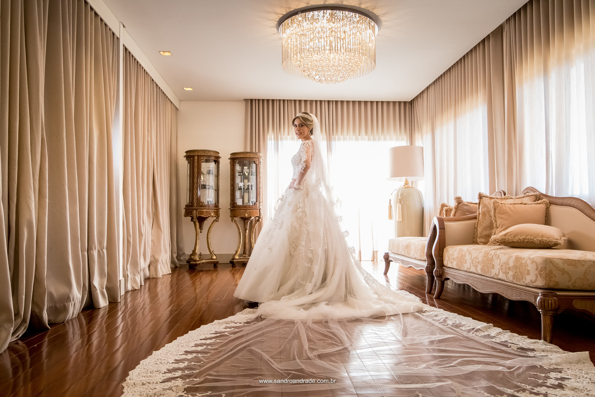 Uma linda imagem atemporal, não marca tempo e nem época, com uma bela composição no hall de atendimento as noivas, com móveis estilo Luiz XV, a noiva está ao centro, um pouco de costas, mostrando seu lindo vestido de noiva, a cauda e o seu lindo véu.