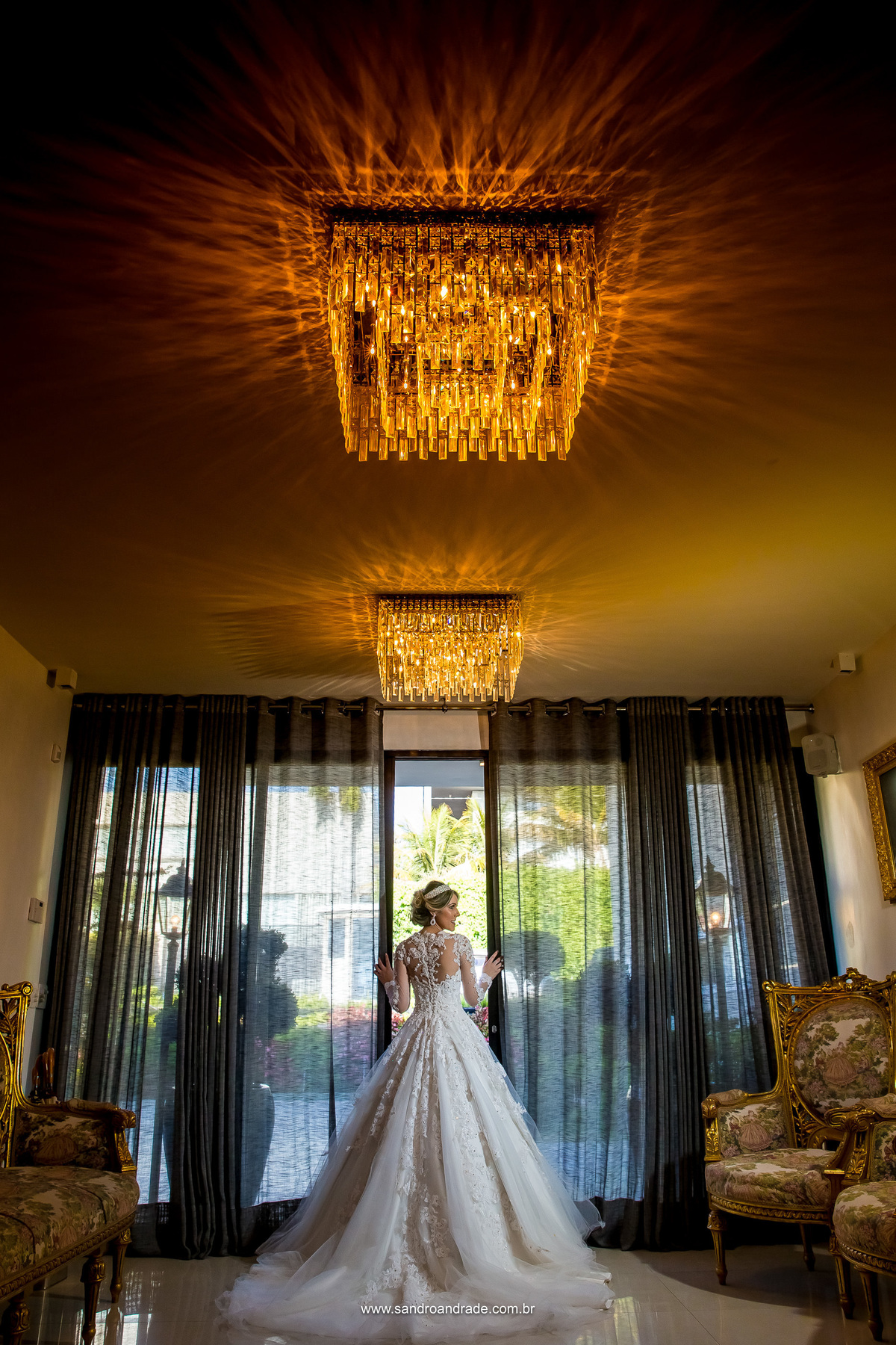 Uma bela fotografia colorida, a noiva a porta, com as mãos apoiada em cada lado e sorrindo feliz. Lindo registro do nosso artista fotógrafo Sandro Andrade, um dos melhores fotógrafos de Brasília e do Mundo.